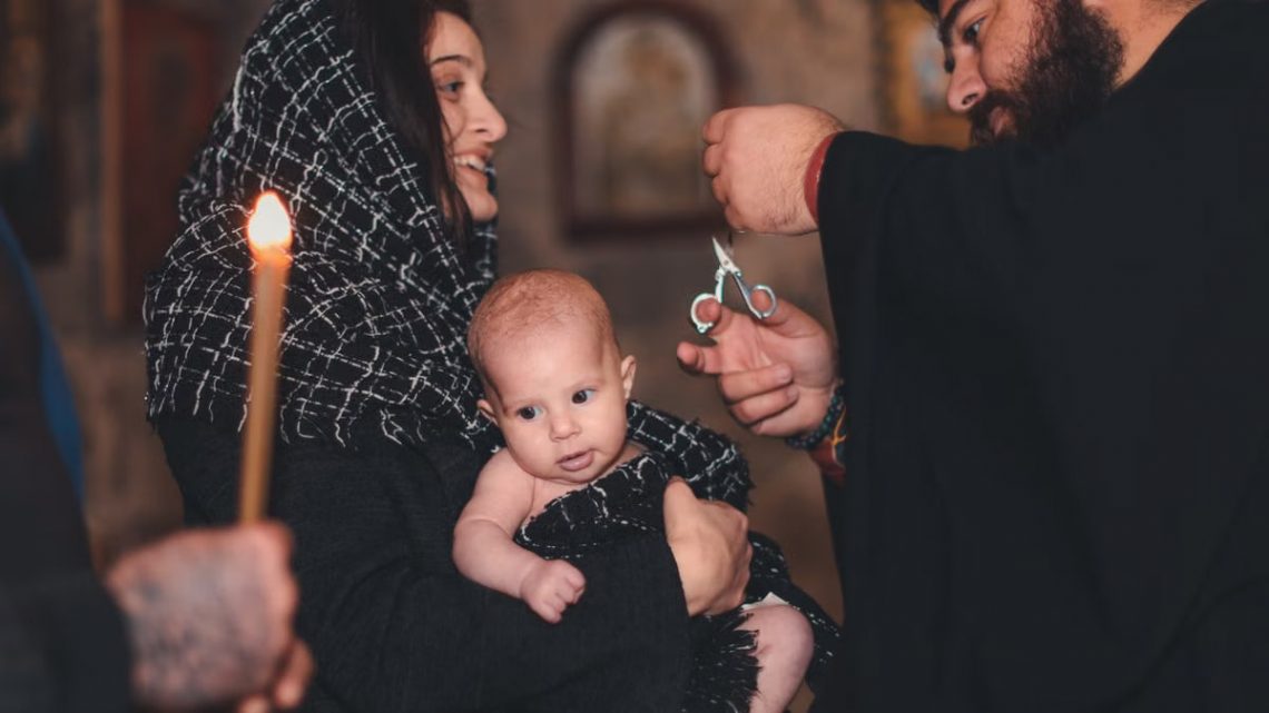 An intimate Orthodox baptism ceremony featuring a priest and family with candle.