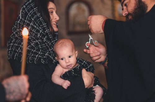An intimate Orthodox baptism ceremony featuring a priest and family with candle.