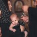 An intimate Orthodox baptism ceremony featuring a priest and family with candle.